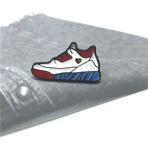 Detail einer bunten Sneaker-Emaille-Anstecknadel mit Herz auf grauem Stoffhintergrund