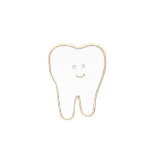 Gros plan d'un pin's en émail blanc en forme de dent avec sourire et bords dorés