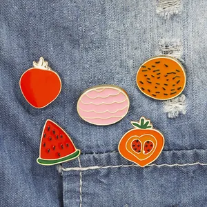 Close-up of five cute fruit enamel pins attached to a blue denim fabric pocket