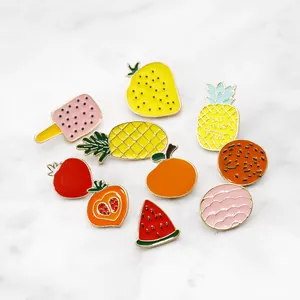 Macro shot of colorful enamel fruit pins including pineapple and watermelon on marble