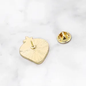 Golden fruit-shaped brooch pin back with butterfly clasp on marble surface