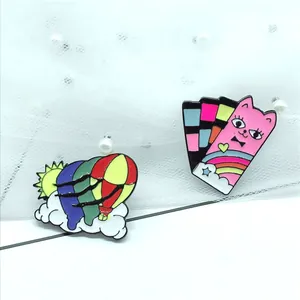 Detailed macro of two colorful enamel pins featuring a hot air balloon and a cartoon cat