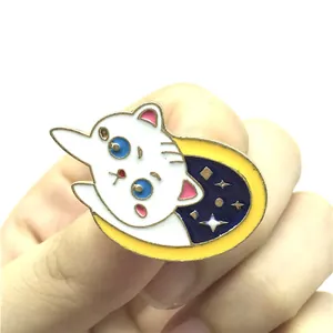 Dettaglio ravvicinato di una spilla in smalto con gatto bianco su una mezzaluna gialla