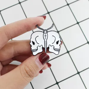 Macro detail of gothic skull butterfly enamel pin held by hand for scale on white background