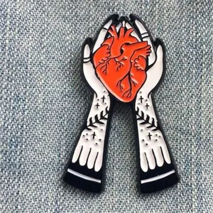 Épingle gothique en émail avec des mains tatouées tenant un cœur rouge réaliste