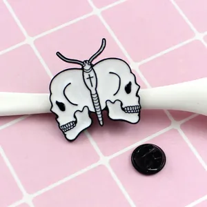 Detail of white butterfly skull enamel pin with cross symbol on pink grid background