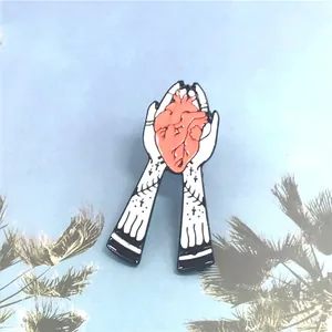 Broche en émail créative avec mains tenant un cœur rose et tatouages gothiques