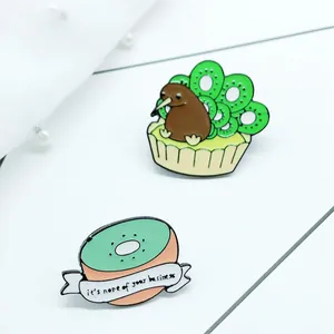 Detail van kiwi-vogel en cake emaille pins met slogan op witte stoffen achtergrond