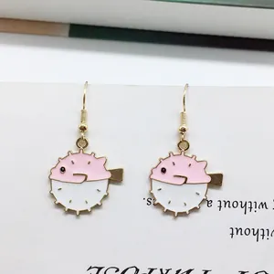 Detail of pink pufferfish earrings with golden hooks on white paper background