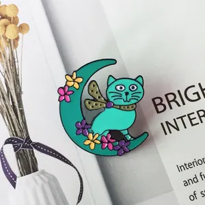 Détail de la broche émail chat et lune croissant vert menthe sur un magazine