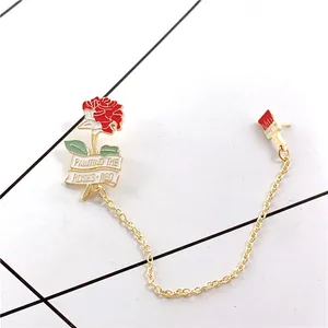 Detail of red rose and paintbrush enamel pins with chain and engraved ribbon