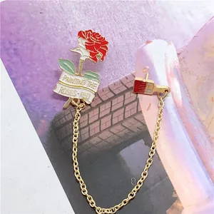Detailed view of red rose and paintbrush chain brooch with 'Painting the Roses Red' text