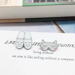 Dettaglio di spillette in smalto con gatto mascherina e pantofola su cartoncino regalo