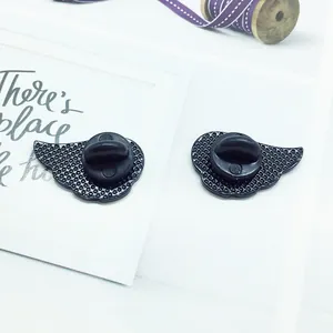 Pair of black cartoon wing pins with rubber backings on decorative paper background