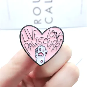 Détail macro de la broche cœur en émail rose avec patte de chat et slogan pour chat