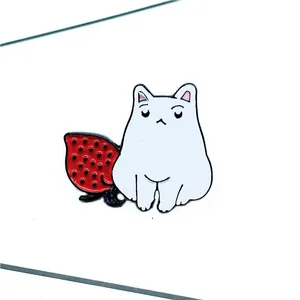 Détail d'un pin's émaillé avec un chat blanc mignon à côté d'une fraise rouge vif