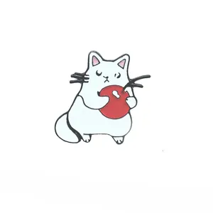 Détail d'un badge émaillé montrant un chat blanc mignon serrant une pomme rouge vive