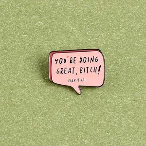 Macro di una spilla in smalto rosa con frase motivazionale su sfondo di carta verde