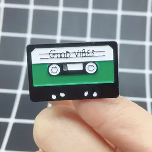 Close-up of retro cassette enamel pin with Good Vibes text on a checkered background