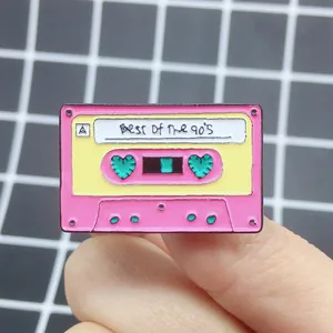 Close-up of retro pink cassette enamel pin featuring heart reels and 90s theme