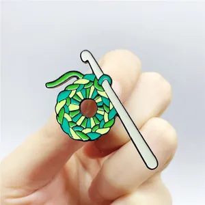 Detail of green knitted wool ball enamel pin brooch being held to show size and scale