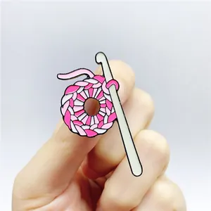 Detailed view of pink and white knitted wool ball enamel pin held in hand for scale