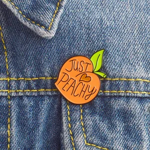 Gros plan détaillé d'un pin's pêche en émail avec texte JUST PEACHY sur une veste en jean