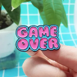 Macro view of Game Over pixel heart enamel pin in pink and blue held by fingers
