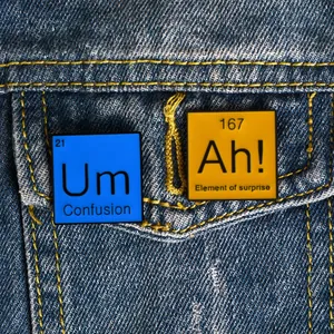 Gros plan des épingles en émail AH et UM sur la poche d'une veste en jean