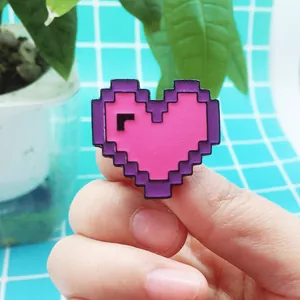 Detail shot of a pixel art heart enamel pin on a hand with vibrant pink and purple colors