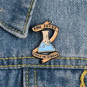 Cute cartoon chemistry beaker enamel pin with Rise Above text on blue denim jacket