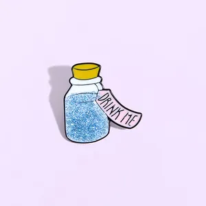 Detailed view of enamel potion bottle brooch with blue glitter and Drink Me tag