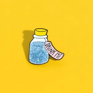 Macro detail of enamel potion bottle brooch with blue glitter and Drink Me tag