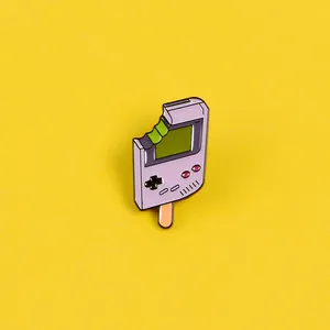 Dettaglio della spilla smaltata a forma di console di gioco e ghiacciolo su sfondo giallo