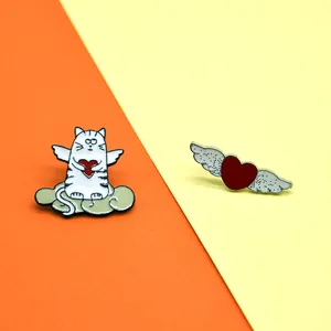Vue macro de pins émaillés chat ange et cœur ailé sur un fond bicolore jaune vif