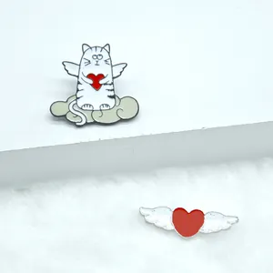 Détail des pin's émaillés chat ange et cœur rouge ailé avec finition métallique brillante