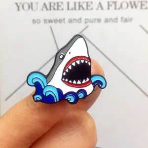 Gros plan d'un pin's requin bleu en émail avec des vagues tenu à la main pour la taille