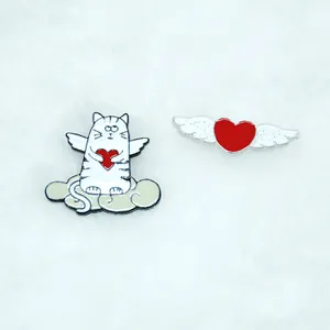Détail de pins émaillés chat ange et cœur rouge sur une texture blanche douce