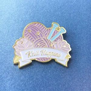 Détail d'un pin's émaillé pelote de laine violette avec texte Knit Happens sur bleu