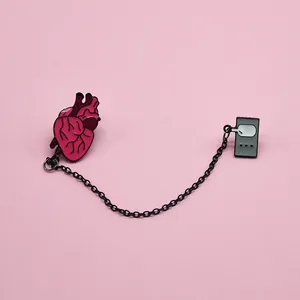 Detailed view of enamel heart and player pin set connected by a black metal chain