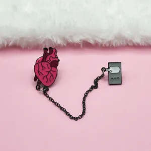 Macro detail of enamel heart brooch connected by a black metal chain on pink background