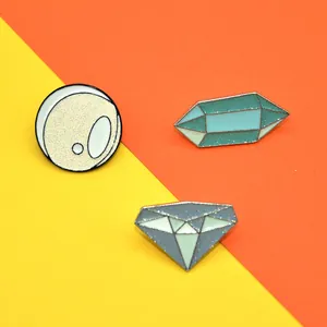 Detail of three geometric enamel pins with glitter finish on a vibrant background