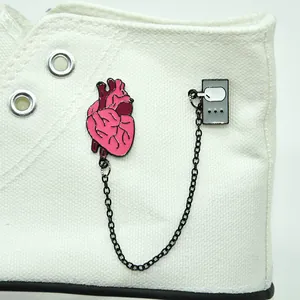 Detail of pink anatomical heart and grey music player enamel chain brooch on white shoes
