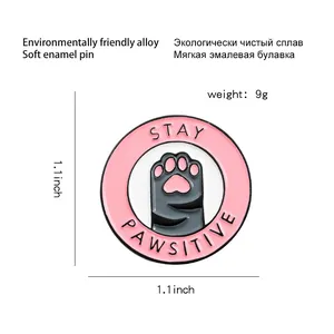 Pin's émaillé Stay Pawsitive patte de chat rose en alliage sur un fond blanc minimaliste