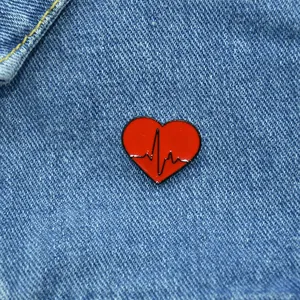 Close-up of a red heart enamel brooch with black EKG pulse line on blue denim fabric