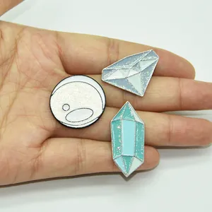 Handheld view of glitter enamel pins featuring cartoon diamond and crystal ball shapes