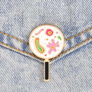 Cartoon Emaille-Pin Lupe mit bunten Mikroben auf blauem Denim-Stoffhintergrund