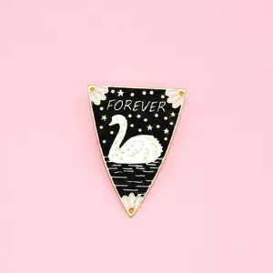 Detail of a triangle enamel pin with white swan and gold stars on a black background