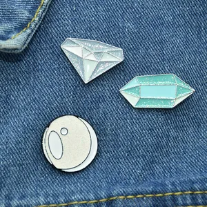 Close-up of sparkling enamel pins featuring diamond and celestial shapes on denim fabric