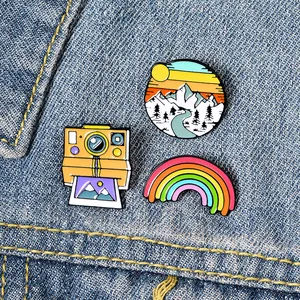 Close-up of enamel pins set featuring a vintage camera, rainbow, and mountain sunset